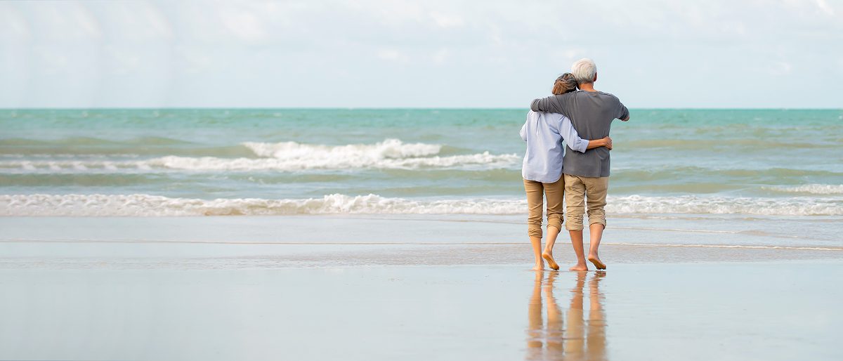 Elderly couple embracing on a sandy beach.