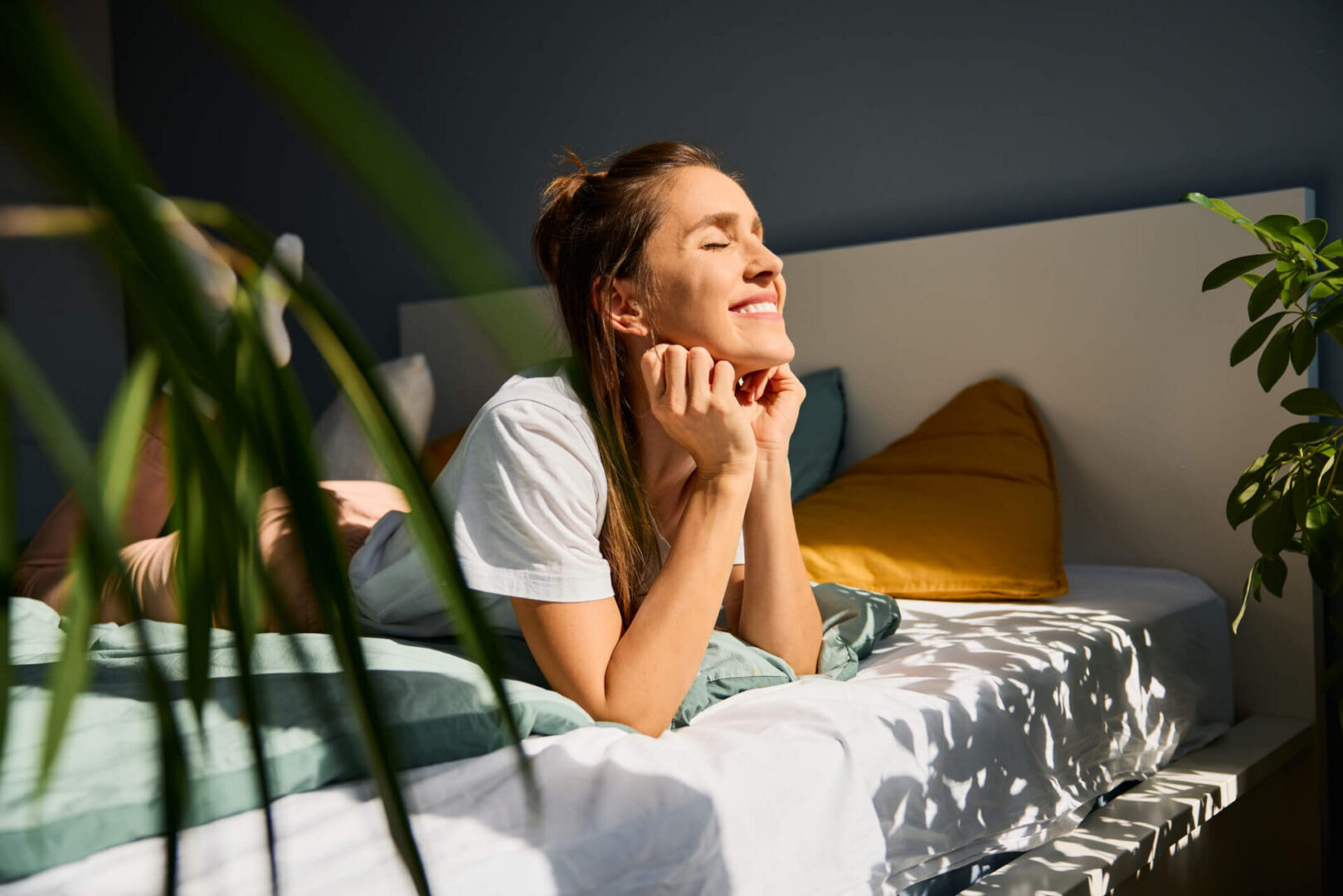 Woman enjoying sunlight on bed, smiling brightly.