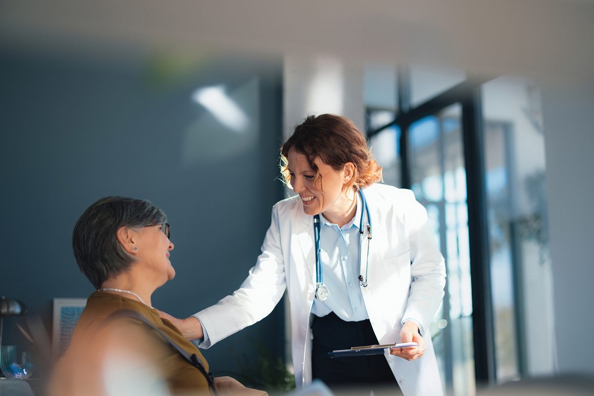 Doctor conversing with seated patient, smiling warmly.