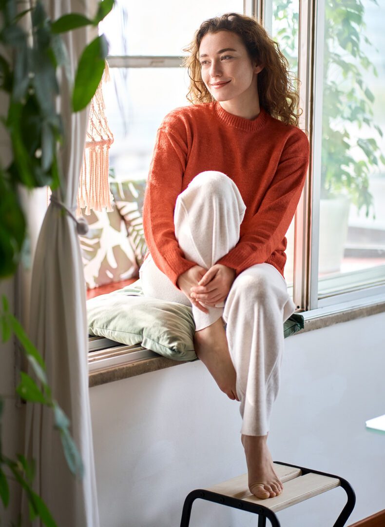 Woman sitting on windowsill, smiling contentedly.
